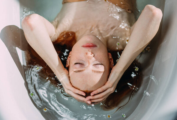 Чувственная женщина с длинными рыжими волосами расслабляется в воде с крошечными цветами