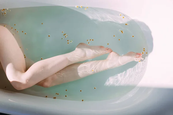 Oříznutý záběr ženských štíhlých nohou ve vaně s čistou vodou a malými květy — Stock fotografie