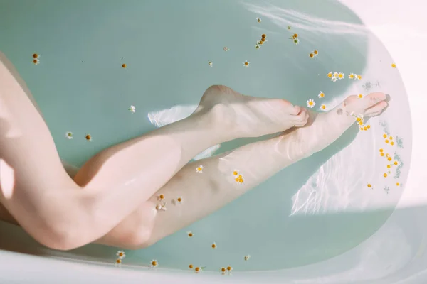 Καλλιεργημένη φωτογραφία από γυναικεία λεπτά πόδια σε μπανιέρα με καθαρό νερό και μικρά λουλούδια — Φωτογραφία Αρχείου