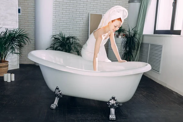 Mujer sonriente sentada en el borde de la bañera corriendo el baño, probando el agua con la mano — Foto de Stock