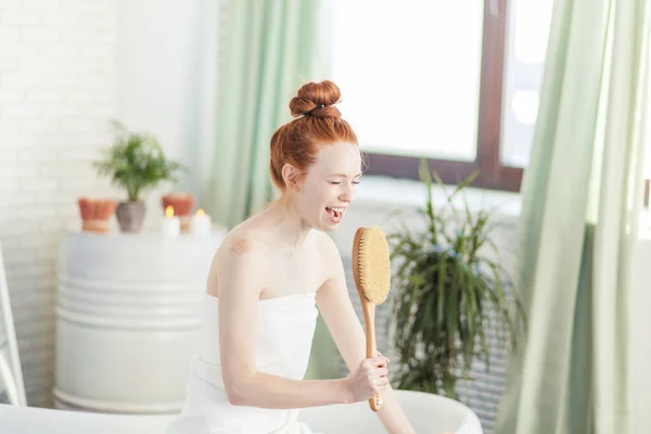 Joyeuse femme chantant en utilisant la brosse comme microphone relaxant dans le bain dans la salle de bain — Photo