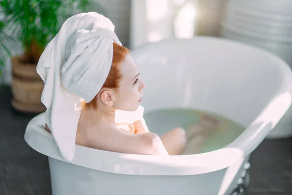 Femme rousse se relaxant dans la baignoire avec mousse dans le centre de spa. — Photo