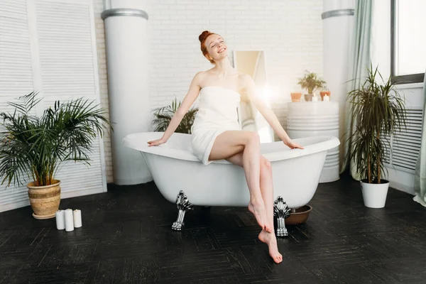 Femme rousse préparant bain en mousse dans une salle de bain spacieuse avec des plantes vertes — Photo