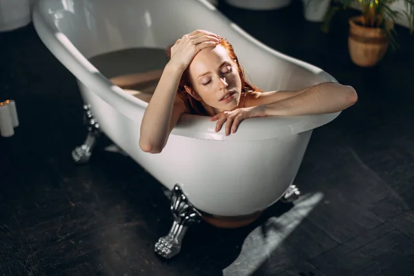 Beautiful seductive young red-haired lady with bare shoulders in bathtub. — Stock Photo, Image