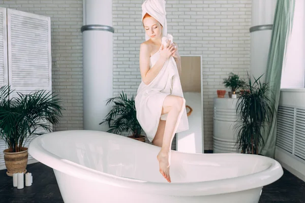 Mujer sonriente sentada en el borde de la bañera corriendo el baño, probando el agua con la mano — Foto de Stock