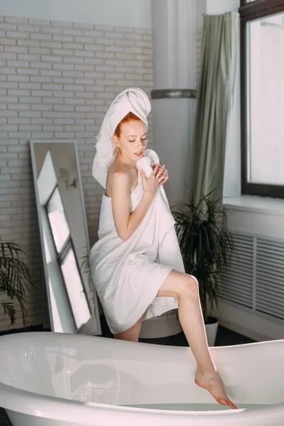 Donna sorridente seduta sul bordo vasca a correre il bagno, testare l'acqua con la mano — Foto Stock