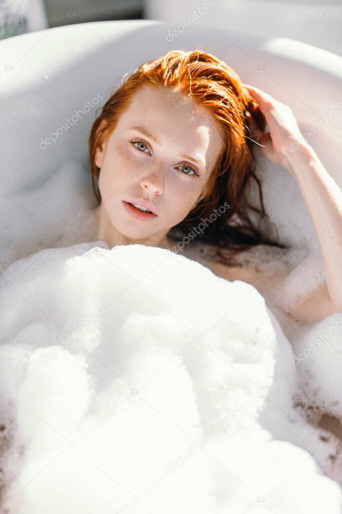 Sensual woman with long ginger hair relaxing in water with tiny flowers