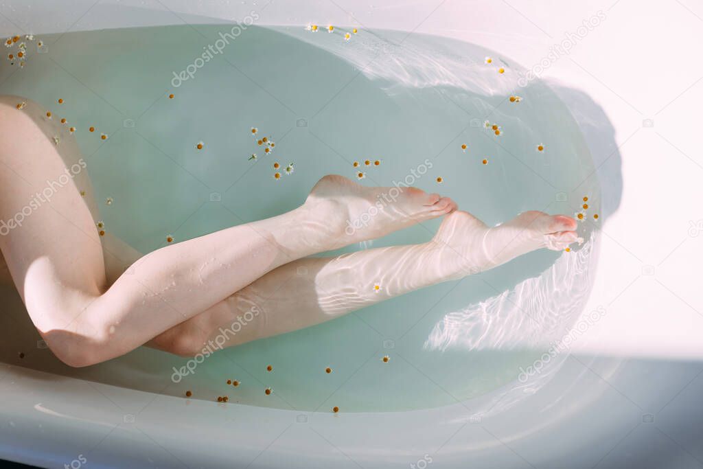Cropped shot of female slim legs in bathtub with clean water and little flowers