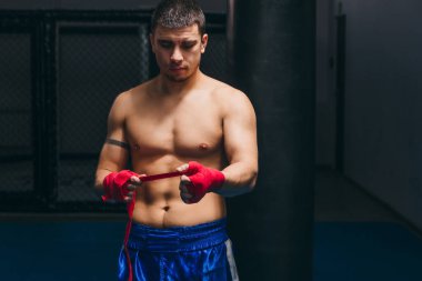 Mavi şortlu gömleksiz erkek boksör, parmaklarını elastik bandajla sarar.