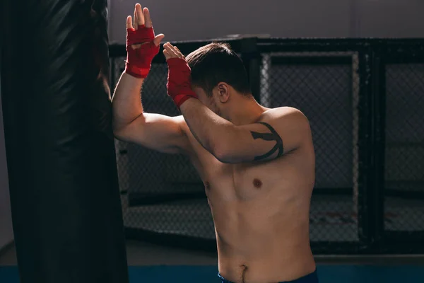 Luchador musculoso practicando con saco de boxeo interior. — Foto de Stock