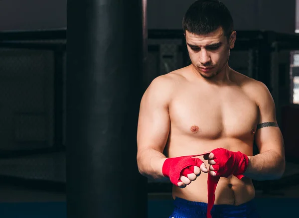Jovem boxeador embrulhando as mãos com bandagem elástica vermelha se preparando para o treino — Fotografia de Stock