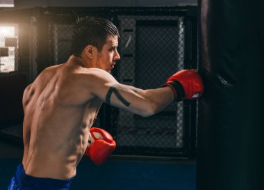 Kırmızı eldivenli erkek boksör kum torbasıyla kardiyo boks yapıyor.