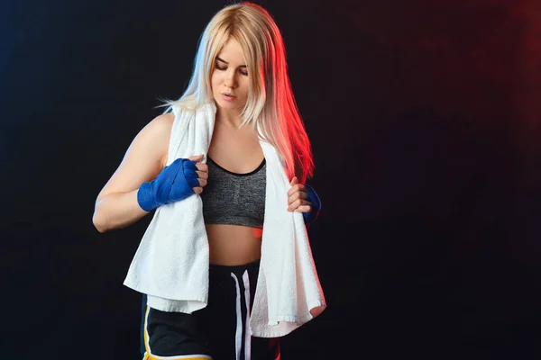 Sporty blonde woman kickboxer fighter with white towel on neck after workout.