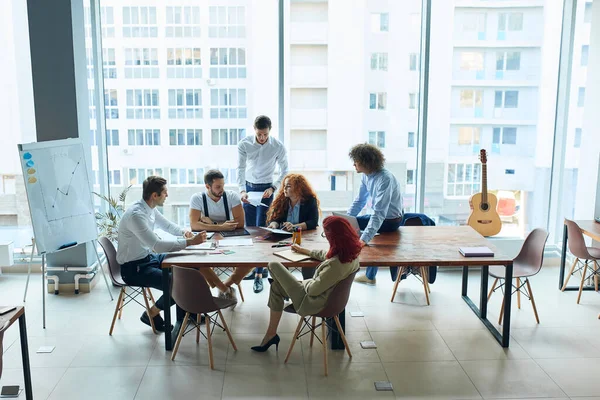 Equipo de negocios de personas caucásicas que trabajan en el interior de oficinas de espacio abierto con ventana panorámica — Foto de Stock