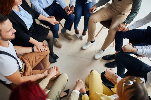 Joven equipo de negocios tomados de la mano mientras están sentados en círculo en la oficina — Foto de Stock