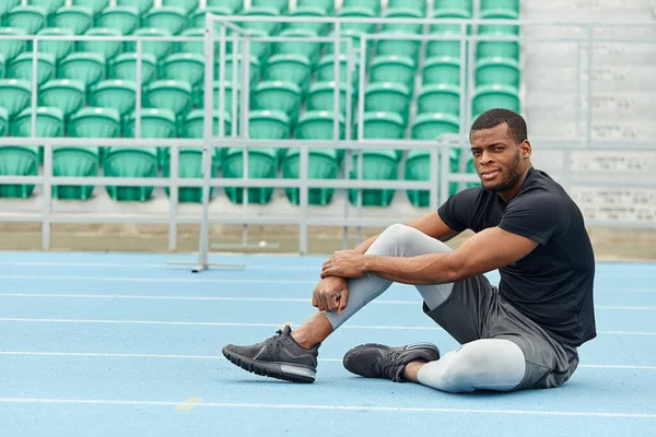 Vyčerpaný mladý sportovec sedící na stadionu a dívající se do kamery — Stock fotografie