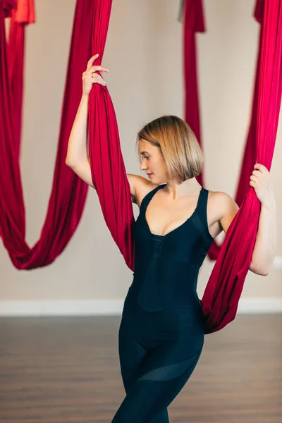 Blonde antigravity yoga instructor standing in empty studio with red hammock. — Stock Photo, Image