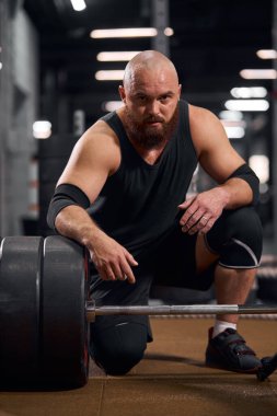 Halterin yanında oturan vücut geliştirici.