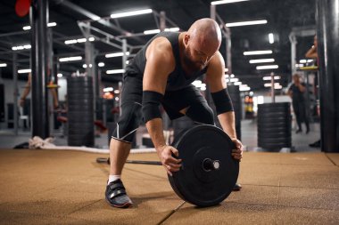 Halter diskini tamir eden kel bir sporcu.