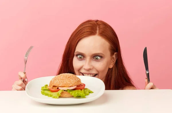 Mujer flaca pelirroja con ojos codiciosos lista para comer hamburguesa. —  Fotos de Stock