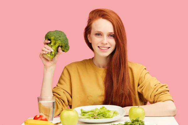 Ładna ruda biała kobieta siedzi przy stole ze zdrowym jedzeniem i brokułami — Zdjęcie stockowe