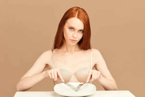 Červenovlasá žena jedla jeden hrášek vidličkou a nožem. Koncepce stravy. — Stock fotografie
