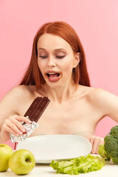 Magersüchtige Frau fühlt sich glücklich, wenn sie Schokolade statt gesundes Gemüse isst. — Stockfoto