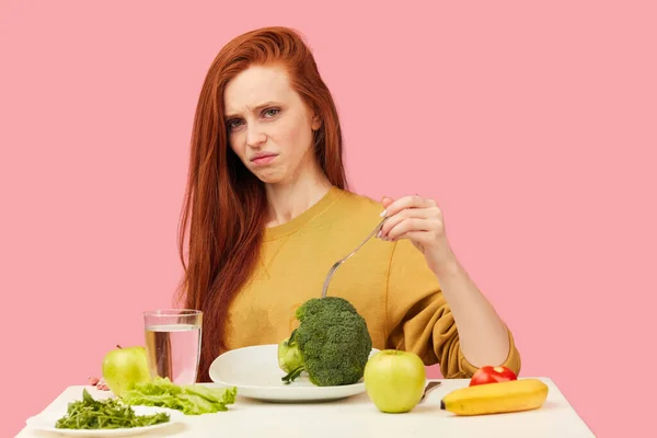 Zeleninová strava. Smutná tupá žena drží brokolici na vidličce, zatímco se šklebí — Stock fotografie