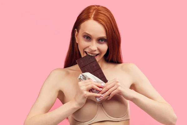 Młoda chuda anorektyczka trzymająca batonik czekoladowy, pozująca na różowo. — Zdjęcie stockowe