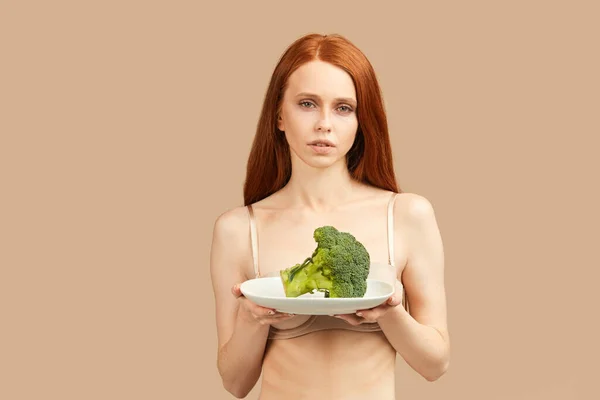 Anoreksik kadın elinde tabakla stüdyoda izole edilmiş çiğ brokoli tutuyor. — Stok fotoğraf