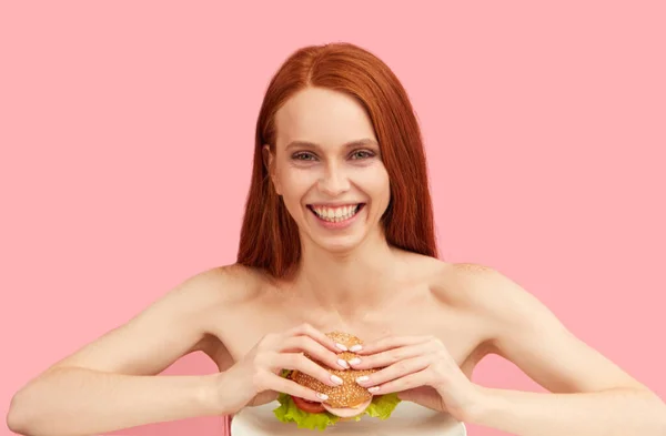 Feliz pelirroja flaca mujer con ojos codiciosos estar listo para comer hamburguesa. —  Fotos de Stock