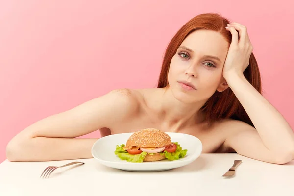 Rudowłosy chudy kobieta z chciwymi oczami jest gotowy do jedzenia hamburgera. — Zdjęcie stockowe