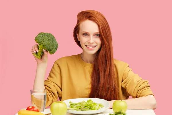 Hübsche rothaarige Kaukasierin sitzt am Tisch mit gesundem Essen und Brokkoli — Stockfoto