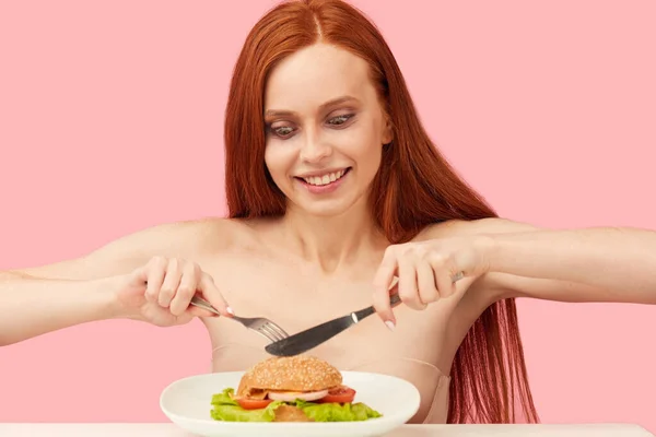 Рудоволоса худа жінка з жадібними очима готується з'їсти бургер . — стокове фото