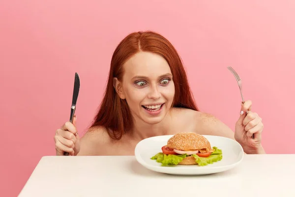 Red-haired skinny woman with greedy eyes being ready to eat burger. — Stock Photo, Image