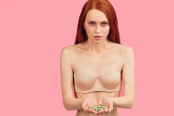 Red-haired anorexic woman in nude underwear eating only slimmimg pill as a diet