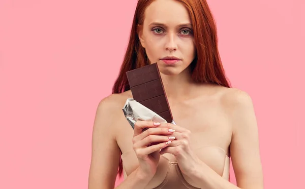 Young skinny anorexic unhealthy woman tempting to eat chocolate bar.