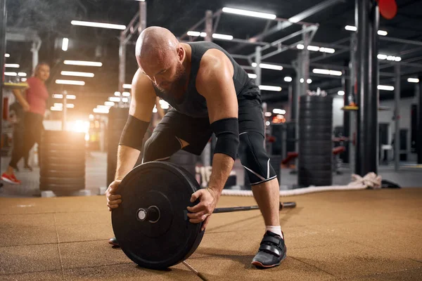 Bald athlete fixing disc of barbell — Stock Photo, Image
