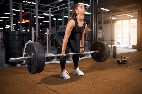 Genç atletik kadın halterle çömeliyor.