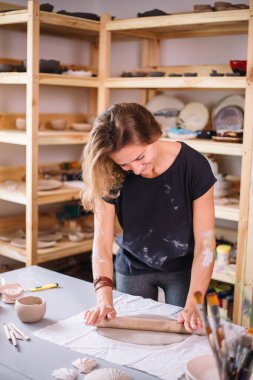 Kadın çömlekçi ustası seramik ürünlerle birlikte masayı topluyor.
