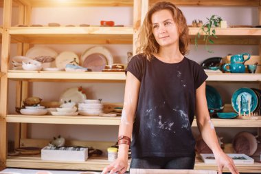 Kadın çömlekçi ustası seramik ürünlerle birlikte masayı topluyor.