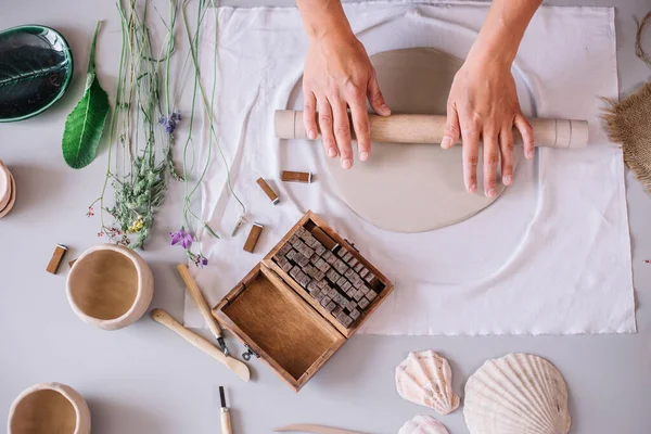Sanatçı, atölye ile kaplı büyük gri oklavayı kullanarak çiğ çamur yuvarlıyor.