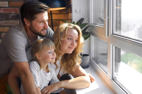 Heureuse jeune famille regardant par la fenêtre à la maison — Photo