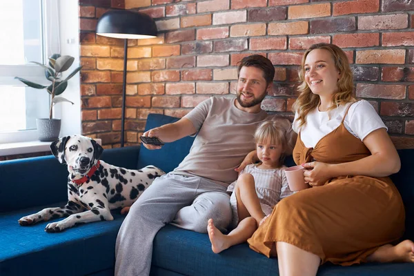 Família feliz atraente com cão assistir tv na sala de estar — Fotografia de Stock