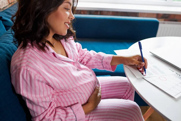 Щаслива вагітна жінка, що пише в календарі вагітності, вдома — стокове фото