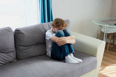 Üzgün çocuk evde tek başına oturup ağlıyor.