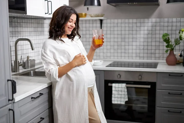 Potret wanita hamil bahagia minum jus segar di dapur — Stok Foto