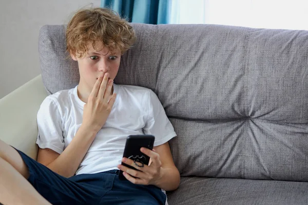 Chico sorprendentemente mira las noticias en el teléfono inteligente — Foto de Stock