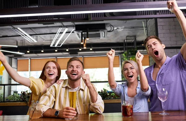 Dos parejas viendo el deporte en la televisión juntos bebiendo cerveza animando al equipo y celebrando — Foto de Stock