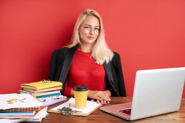 Ofis masasında dizüstü bilgisayar ve kağıtlarla oturan kendine güvenen beyaz kadın portresi.